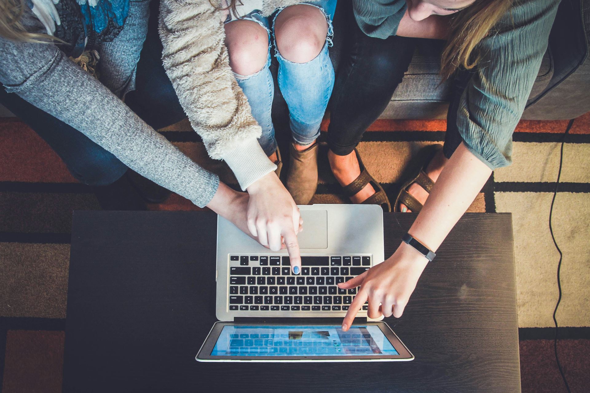 a laptop on a table with several people pointing at the screen